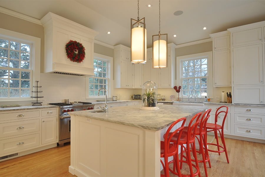 Transitional kitchen with white cabinetry, marble countertops, light hardwood flooring, and vibrant red metal hi-top chairs