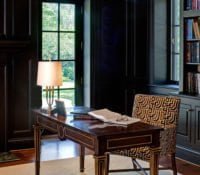 Transitional office space with ornate wood desk table with gold trim, black cabinetry, black and gold cushioned chair, and medium hardwood flooring