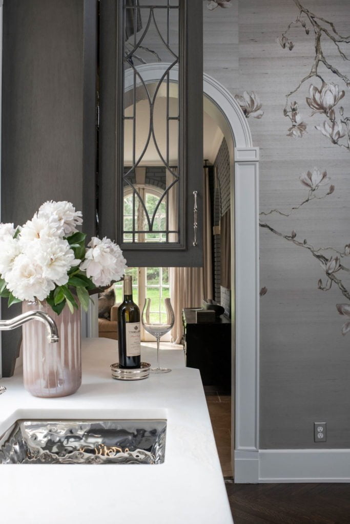 Custom dark grey cabinetry above white marble countertops and minimal floral wallpaper