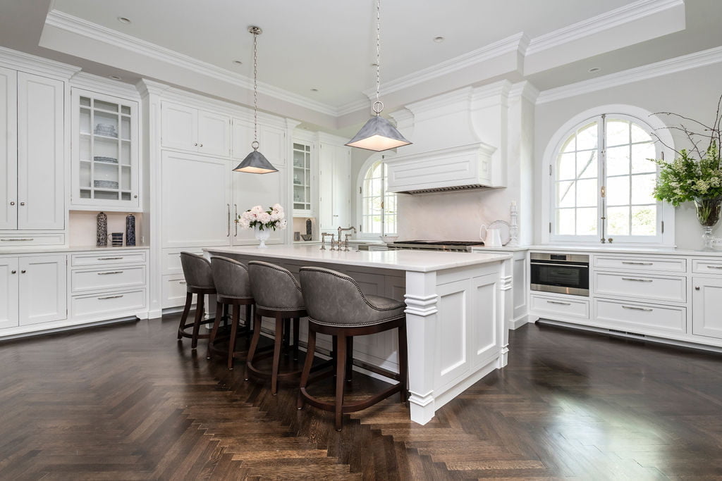 Custom white cabinetry with dark chevron hardwood flooring and off-white wall color, grey leather hi-top chairs (Other side)