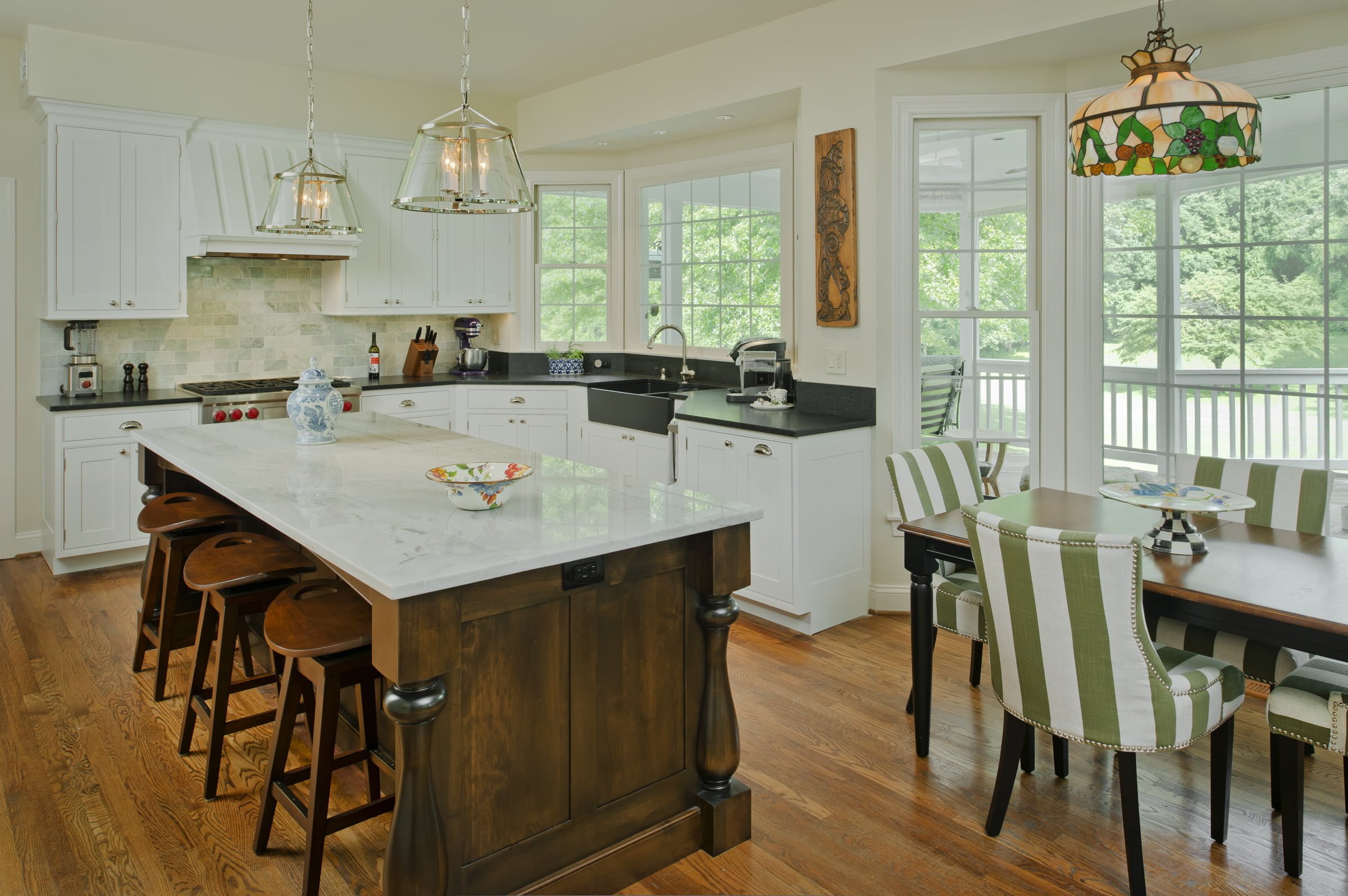 Transitional kitchen with medium hardwood flooring, white cabinetry, dark marble countertops and dark wooden island and stools