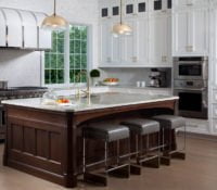 Transitional kitchen island with custom white cabinetry, dark hardwood island , granite countertops and leather stools, and a silver and gold trim