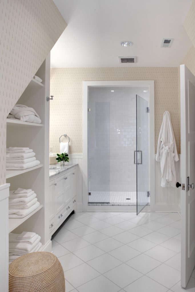 Transitional bathroom with diagonal white tile flooring, minimal patterned cream wallpaper, and glass shower door