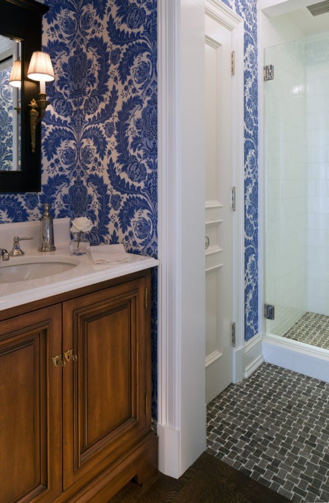 Interior doorway from sink to shower room with blue patterned wallpaper and antique-finish wooden drawers