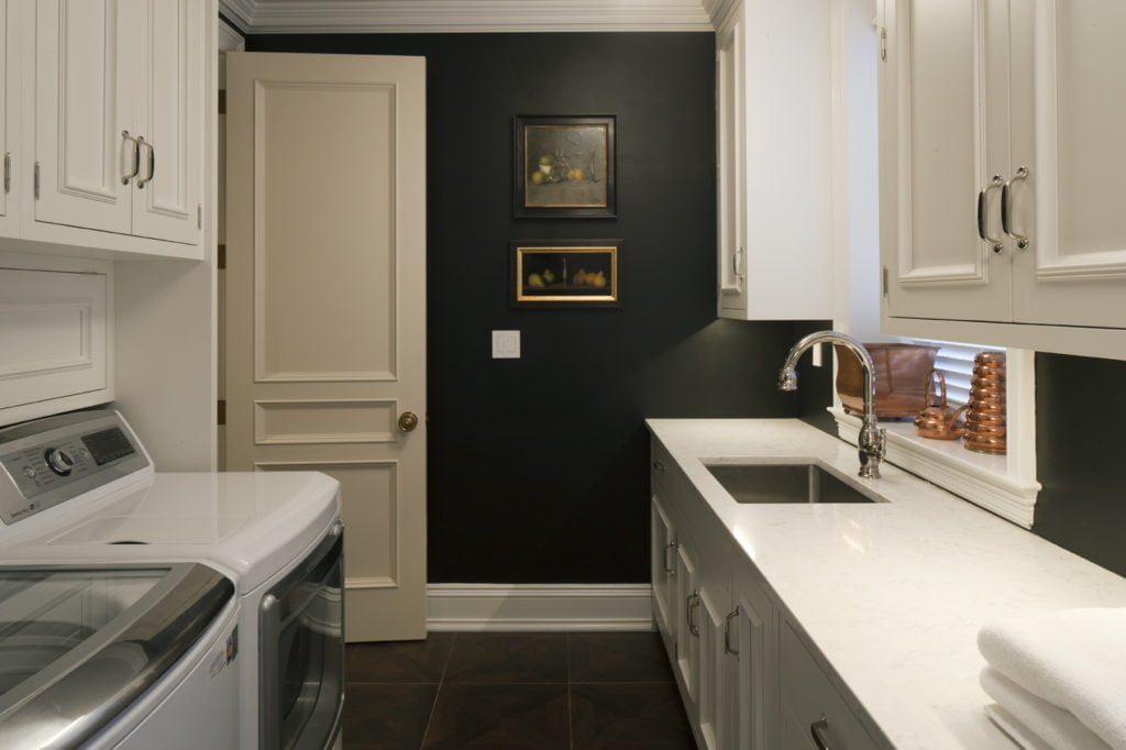 Transitional white cabinetry in black wall and floor tile laundry room and marble countertops