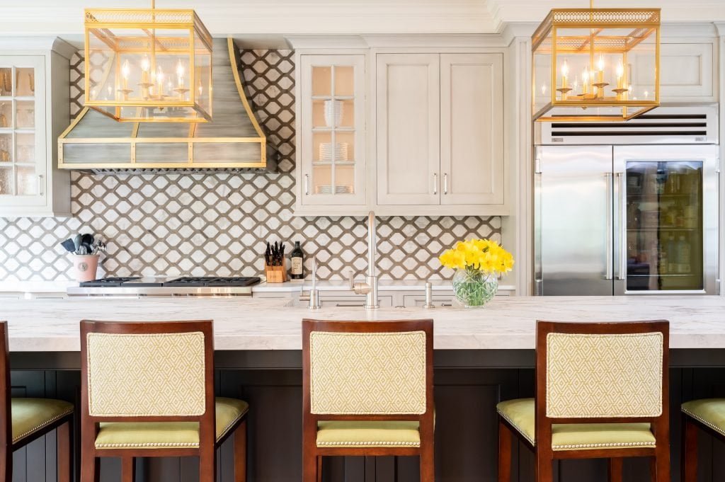 Transitional kitchen with hi-top chairs on island, decorative tile backsplash, and accented gold metal