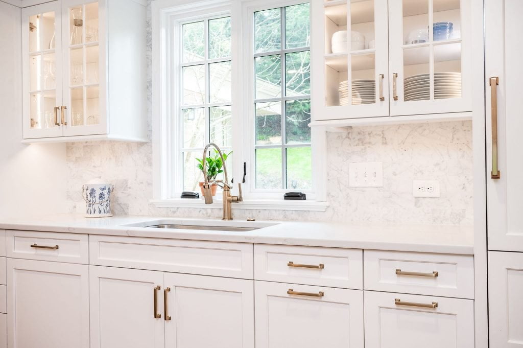 Transitional kitchen sink with white cabinetry, gold accents, and marble countertop and backsplash (Zoomed in)