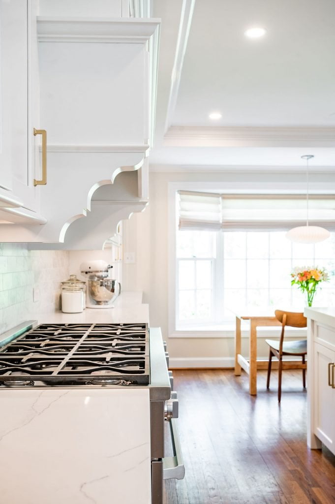 Transitional kitchen stovetop with white marble countertops and decorative molding on the hood vent