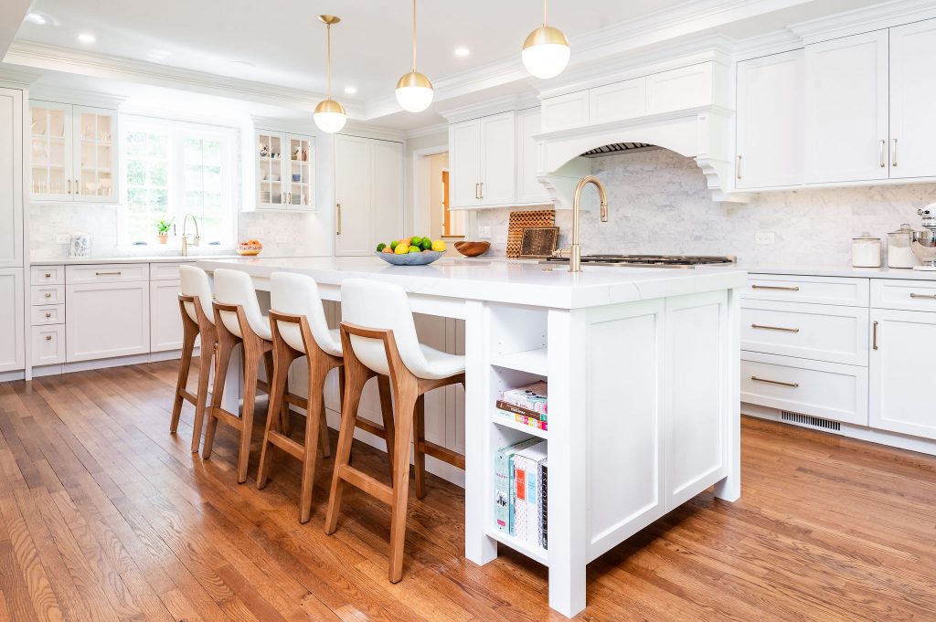 Transitional kitchen island with white cabinetry and marble countertops, and matching wooden hi-top chairs with white leather seats