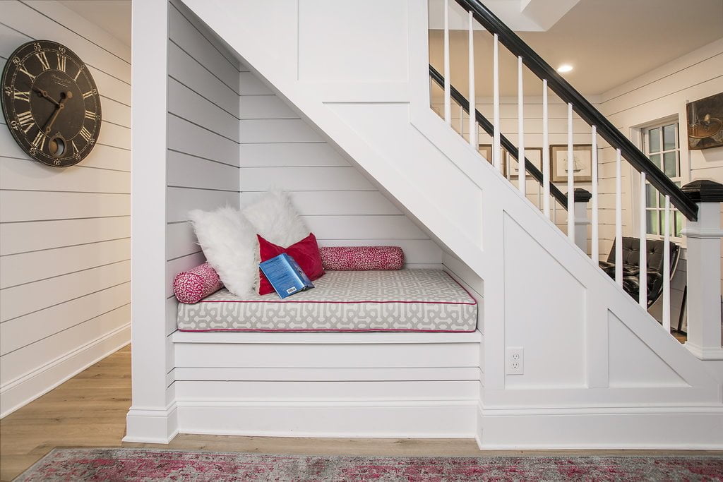 Triangular sitting nook with white paneling and cushions underneath staircase