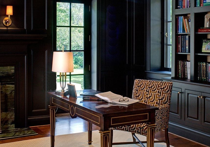 Transitional office space with ornate wood desk table with gold trim, black cabinetry, black and gold cushioned chair, and medium hardwood flooring