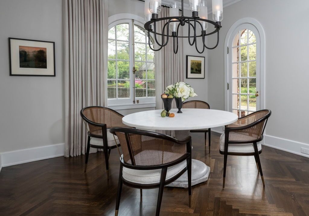 Remodeled dining area with a modern chandelier, dining table and chairs with dark wood chevron flooring and arched windows