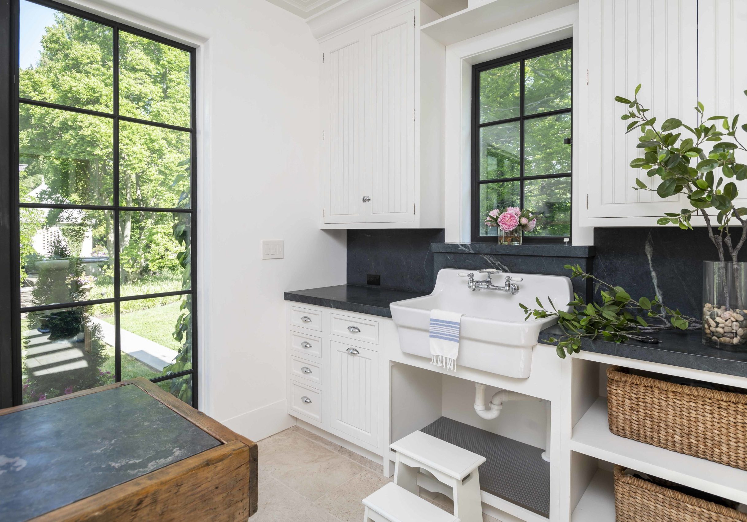 Coastal style washroom with white paneled cabinetry, dark granite countertops, and a dark metal window and door accent (2)