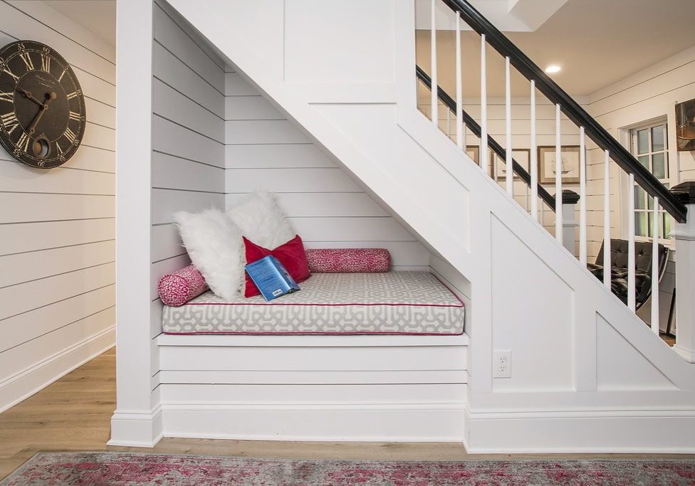 Triangular sitting nook with white paneling and cushions underneath staircase